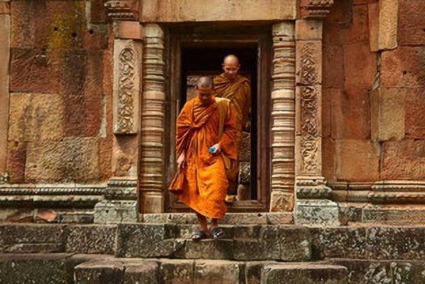 Two Buddhist monks in saffron robes walking through the stone entrance of an ancient Khmer temple in Northeast Thailand.