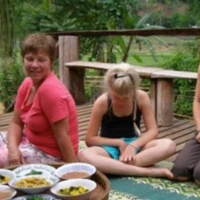 Day 2: Sharing a traditional Karen dinner on a wooden deck overlooking the rice paddies – the kind of genuine connection that defines the CBT homestay experience. A group of international travelers sitting on a wooden porch with a local host, enjoying traditional snacks.