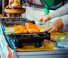 A tasty alternative: Discovering the authentic flavors of Northern Thai street food. A local vendor grilling traditional Thai pork skewers on a charcoal grill at a vibrant street market.