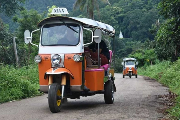 Orange tuk-tuk driving along a scenic jungle road in Northern Thailand