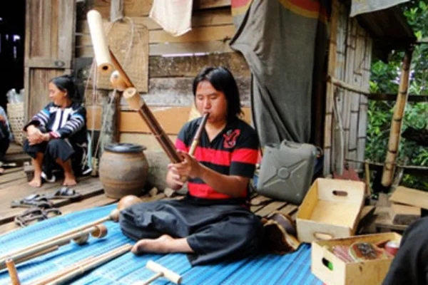 A local hill tribe man playing a traditional musical instrument made of bamboo at a village homestay.